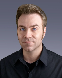 Image of Dr. Ryan Carney, a white man with blue eyes and brown hair with sideburns, wearing a black collared shirt.