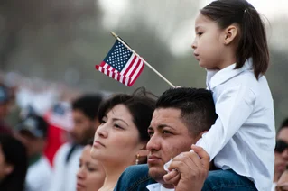 girl sitting on father's shoulders with American flag