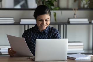 woman smiling looking at computer and holding papers