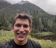 Dr. Philip Brodrick stands before a mountainous and forested landscape.