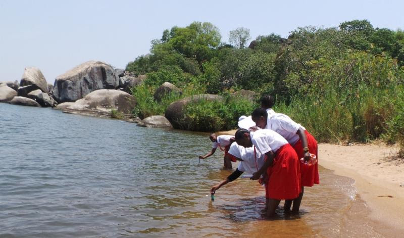 Four people are crouching at a river. Two of them are dipping objects into the water.