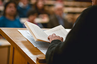 Staff on a central podium delivering a lecture with an open book