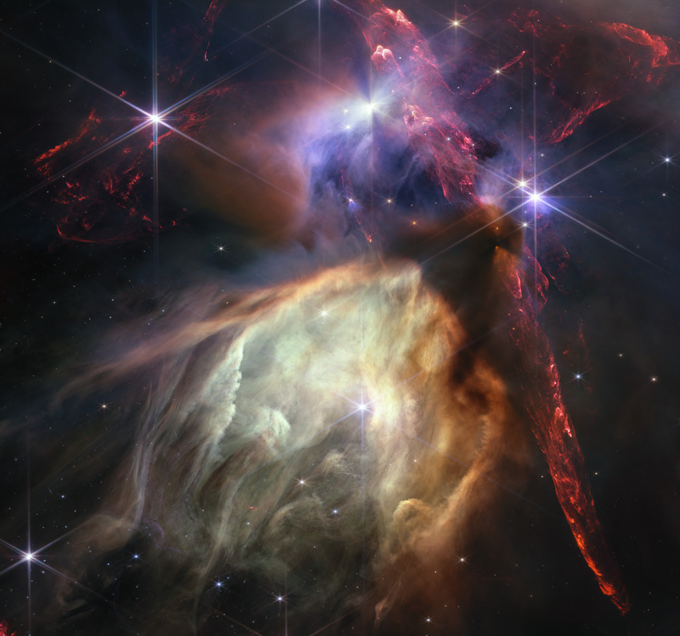 The first anniversary image from NASA’s James Webb Space Telescope displays star birth like it’s never been seen before, full of detailed, impressionistic texture. The subject is the Rho Ophiuchi cloud complex, the closest star-forming region to Earth. It is a relatively small, quiet stellar nursery, but you’d never know it from Webb’s chaotic close-up. Jets bursting from young stars crisscross the image, impacting the surrounding interstellar gas and lighting up molecular hydrogen, shown in red. Some stars display the telltale shadow of a circumstellar disk, the makings of future planetary systems.  The young stars at the center of many of these disks are similar in mass to the Sun, or smaller. The heftiest in this image is the star S1, which appears amid a glowing cave it is carving out with its stellar winds in the lower half of the image. The lighter-colored gas surrounding S1 consists of polycyclic aromatic hydrocarbons, a family of carbon-based molecules that are among the most common compouds found in space. Download the full-resolution version from the Space Telescope Science Institute.  Credit: NASA, ESA, CSA, STScI, and K. Pontoppidan (STScI). Image Processing: A. Pagan (STScI)