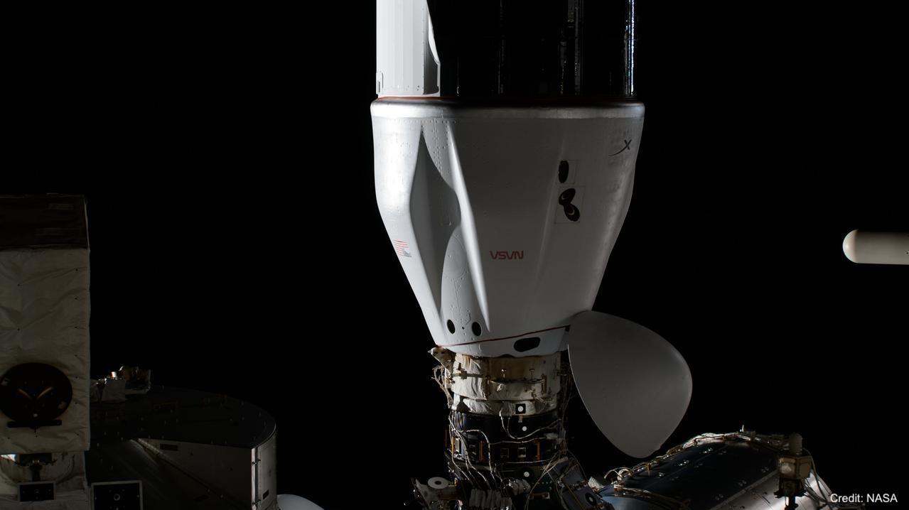 In this photograph, the CRS-30 cargo mission is shown docking with the International Space Station. Against a black background, a white cone — the cargo mission — is attached to a cylinder with a whitish top. There are boxes in the foreground. The image is watermarked, “Credit: NASA.”