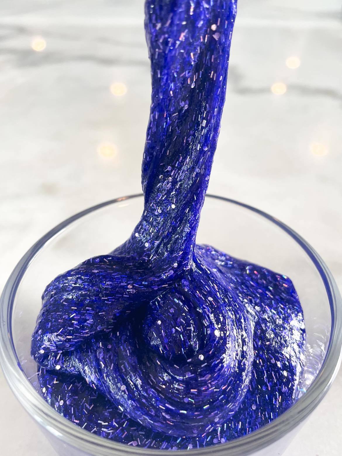 A bowl of homemade swirling, glittery bluish-purple goop: Stardust Slime. The slime fills the bowl, but a portion is being lifted upward as well, highlighting the silver glitter embedded within. Credit: NASA/Ashley Balzer