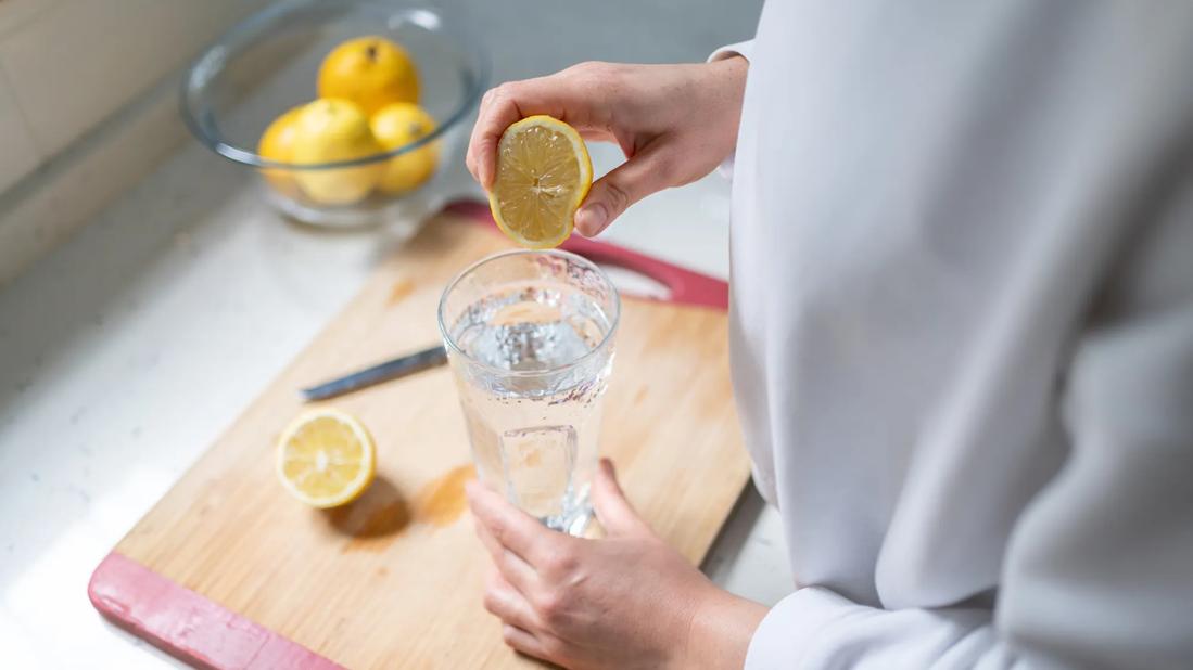 Person squeezing half a lemon into a glass of water