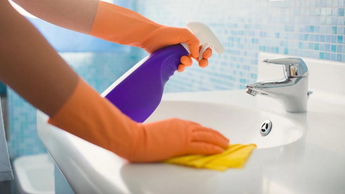 Gloved hands cleaning bathroom sink with spray bottle