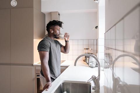 Person with earbud in standing at kitchen sink drinking a glass of water