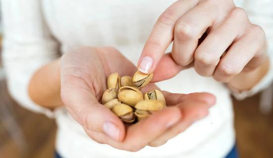 Hand holding pile of pistachios, with other hand picking one up