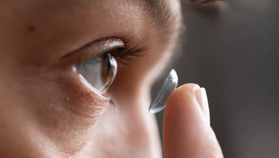 Person holding contact lens on finger up to their eye