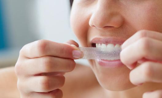 Person applying teeth whitening strip to their teeth