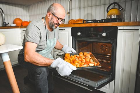 Person wearing oven mitts removing a baking sheet of vegetables from the oven