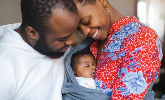 Smiling new parents holding swaddled newborn baby