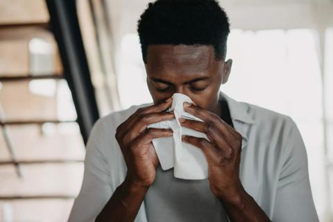 Adult male hunched over blowing his nose into a tissue