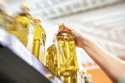 Person lifting bottle of olive oil off grocery store shelf