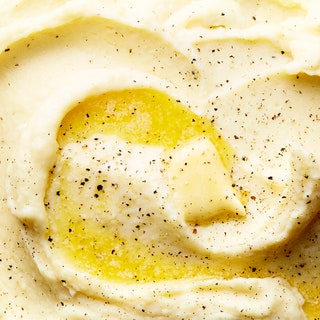 Mashed potoes swirled into a serving bowl topped with melting butter and black pepper.