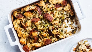 Classic homemade Thanksgiving stuffing with craggy torn bread and herbs in a white baking dish with one serving on a...