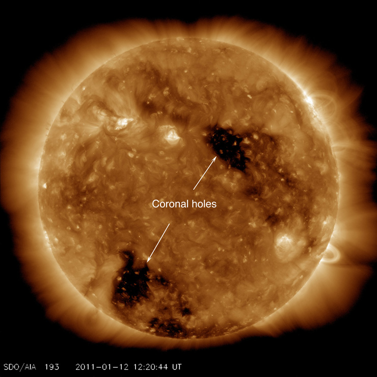 A large, detailed image of the sun in a yellowish light shows texture and two large black spots across the surface. A label marks them "coronal holes."