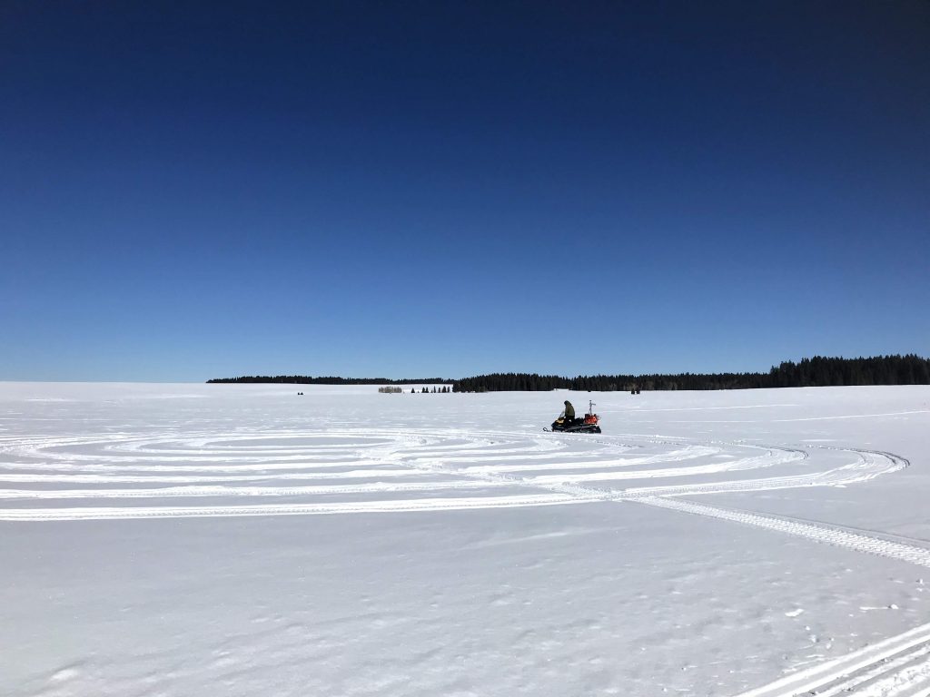 SnowEx 2020 project scientist Hans-Peter (HP) Marshall drives his snowmobile in a tight clockwise circle called a “radar Hiemstra spiral”, taking active radar measurements of the snow. The Twin Otter aircraft carrying SWESARR will later fly over this circle and take similar measurements. Credit: NASA / Jessica Merzdorf