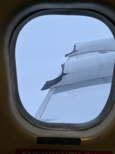 View out a plane window over the wing. The sky is entirely gray as the plane flies through a storm cloud.