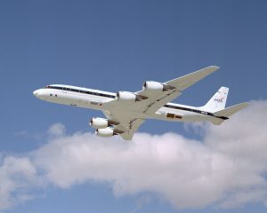 Photo of NASA's DC-8 airplane flying in the sky near a puffy white cloud.