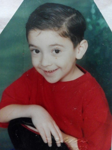 Alt Text: A portrait of a young Nestor Cano. He smiles with his hair parted and wearing a red shirt. 