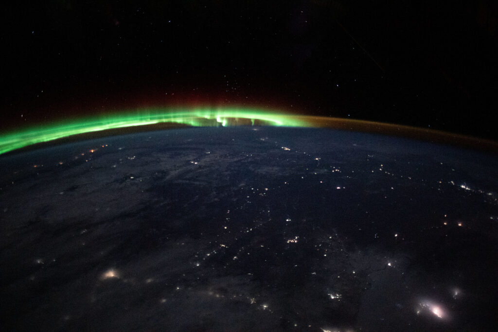 An aurora dances in the horizon of Earth's atmosphere as city lights shine through clouds cast over Mongolia while the International Space Station orbited 263 miles above.