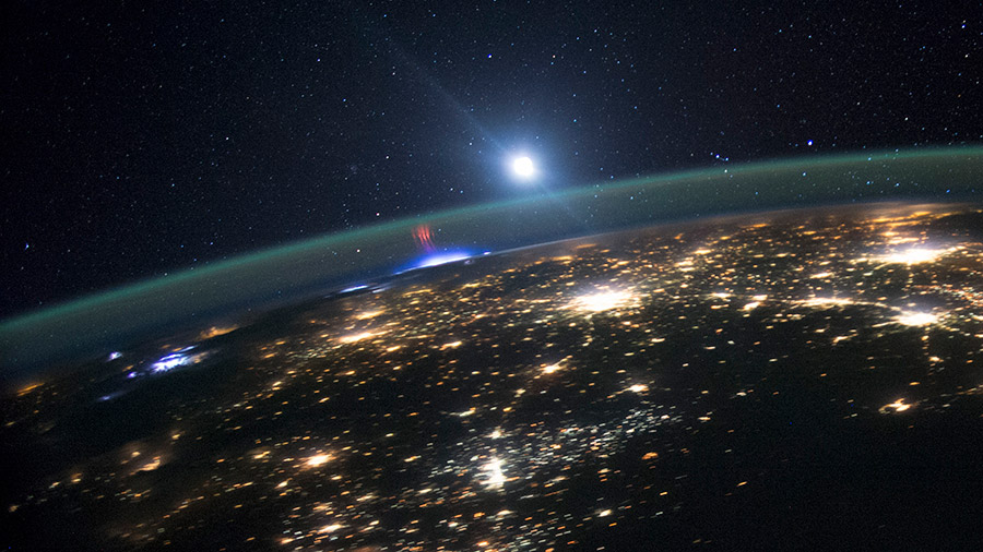 A red sprite is pictured above the white light of an active thunderstorm as the space station orbited above North America in August of 2015.