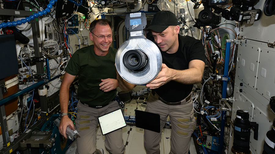 Astronauts (from left) Nick Hague and Matthew Dominick check out a camera and its lighting hardware aboard the International Space Station.