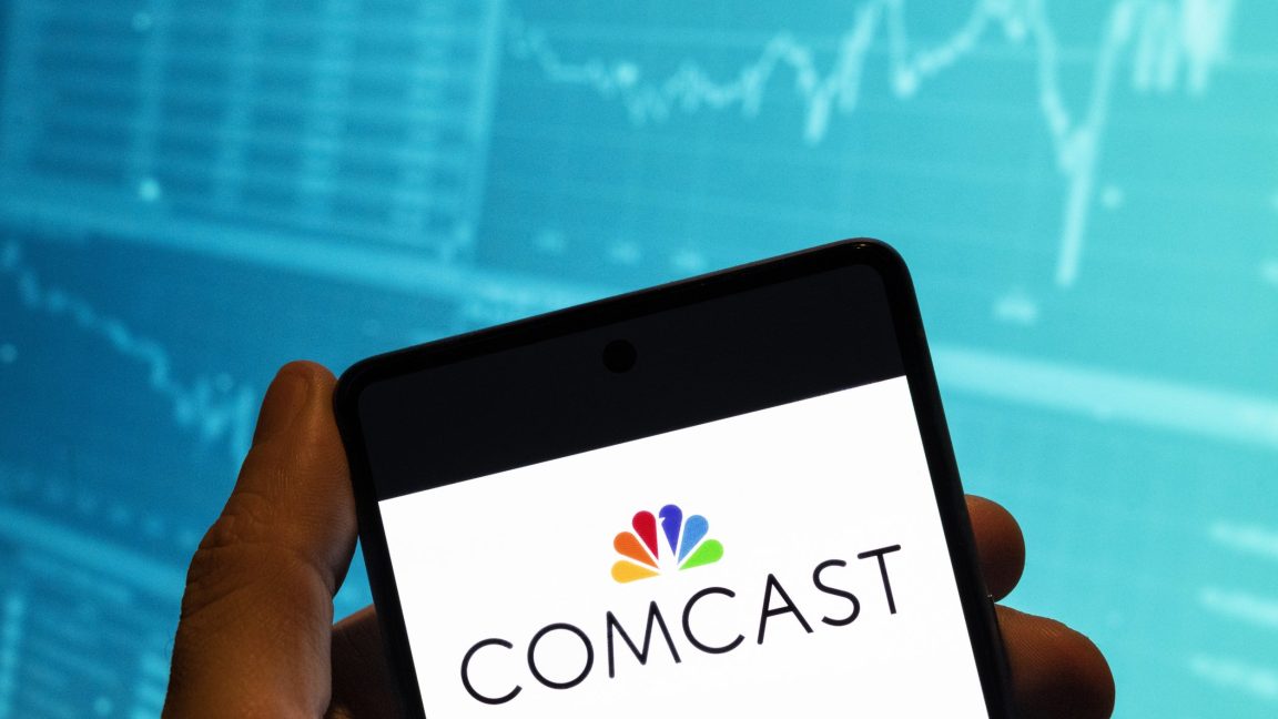 In this photo illustration, the Comcast logo is displayed on a smartphone with a stock exchange index graph in the background.