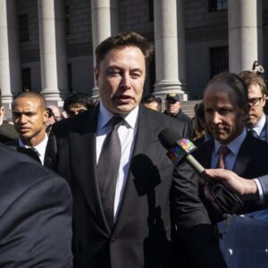 Elon Musk walks out of a federal courthouse and speaks to reporters as a member of the media holds a microphone.