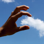 A hand acting as if it can grasp a cloud in the sky, shot from an angle to make it look real.