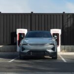 A Polestar 2 EV parked in front of a bank of Tesla Superchargers