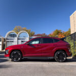 A red Hyundai Kona Electric seen in profile with midcentury townhouses in the background.