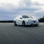 A camouflaged Mercedes CLA prototype driving on a test track