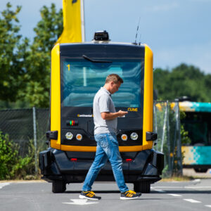 An electrically powered Cube minibus drives toward a man looking at his smartphone.