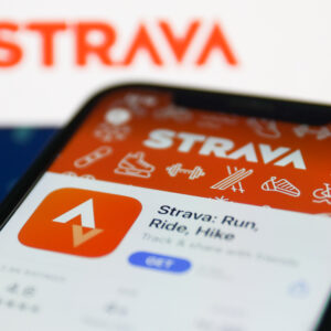 Strava on App Store displayed on a phone screen and Strava website displayed on a screen in the background