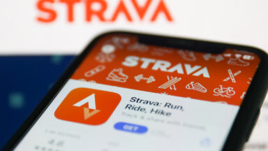 Strava on App Store displayed on a phone screen and Strava website displayed on a screen in the background