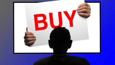 Someone watching a TV that has hands coming out of it which are holding a sign that says "BUY."