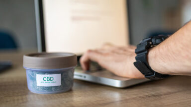 Hands typing on a laptop, next to a container that reads "CBD"