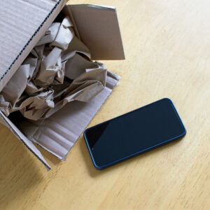 Phone just out of a cardboard box with paper stuffing, on a wood desk.