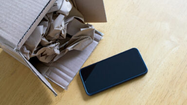 Phone just out of a cardboard box with paper stuffing, on a wood desk.