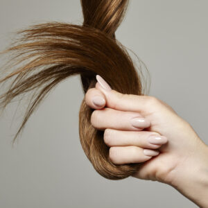 Woman holding hair against a gray background.