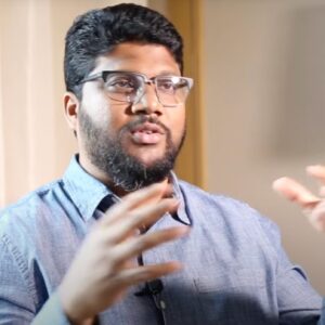 Indian man with beard in blue dress shirt gesturing as he talks