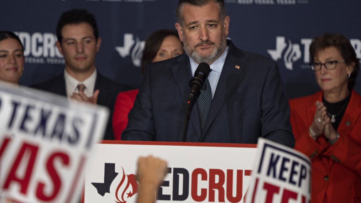 Ted Cruz stands in front of a microphone surrounded by supporters and Ted Cruz signs