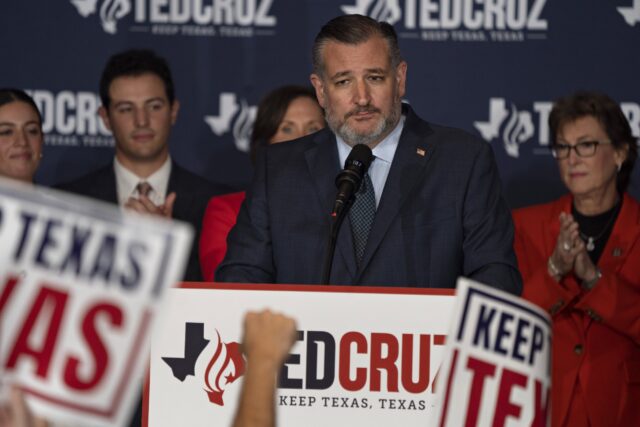 Ted Cruz stands in front of a microphone surrounded by supporters and Ted Cruz signs