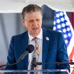 Rhode Island Gov. Dan McKee speaks during a news conference from behind a podium and two microphones, with an American flag in the background.