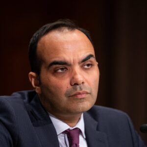 CFPB Director Rohit Chopra sits in front of a microphone while testifying during a Senate committee hearing.