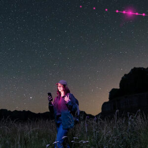 Photo illustration shows a woman holding a phone in a remote area, with dots in the sky to represent satellite service.