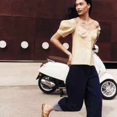 Woman crossing the street wearing neutral tailored outfit from The Outnet, with motorbike in background